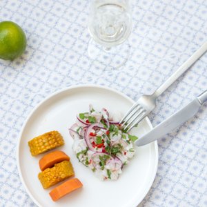 Der Fischsalat auf dem Teller wird von einer Gabel und einem Messer begleitet, während frische Zutaten wie Limette und Chili sichtbar sind.