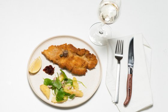 Auf dem Teller befindet sich ein goldbraun gebratenes Schnitzel, umgeben von einem bunten Salat und einer Zitronenscheibe.