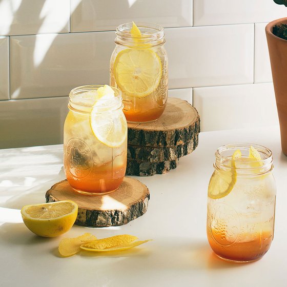 Drei Gläser mit einem erfrischenden Getränk, garniert mit Zitronenscheiben, stehen auf Holzscheiben.