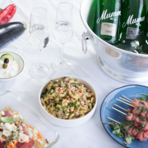 Eine ansprechende Präsentation von Speisen, darunter ein bunter Salat, Spieße und Sektflaschen, die eine festliche Stimmung erzeugen.