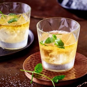 Zwei Gläser mit einem erfrischenden Getränk, gefüllt mit Eis und frischen Minzblättern, auf einem rustikalen Tisch.