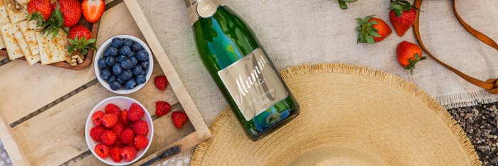 Ein Picknick-Setup mit Sekt, frischen Früchten und Crackern, umgeben von einer natürlichen Umgebung und einer gemütlichen Decke.