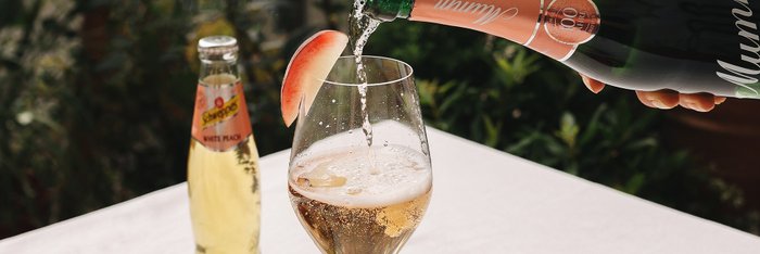 Ein elegantes Glas wird mit Sekt gefüllt, während ein Apfelschnitz dekorativ am Rand sitzt, neben einer Flasche Schorle.