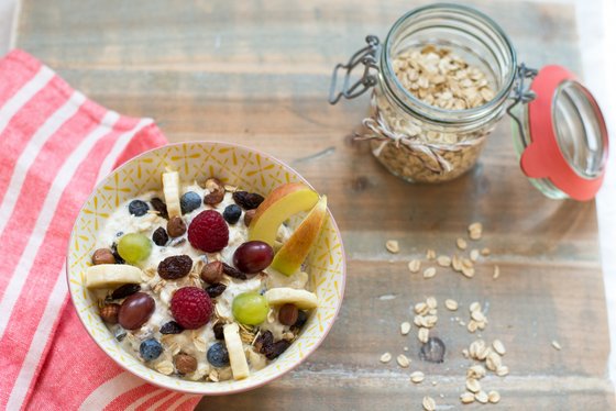 In einer hübschen Schüssel liegen Joghurt, Nüsse und verschiedene Früchte, während ein Glas Haferflocken im Hintergrund steht.