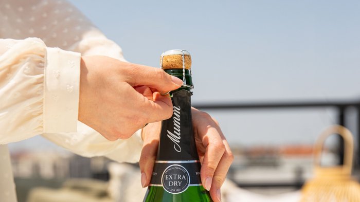 Die Person entfernt den Drahtverschluss von einer Flasche Mumm Extra Dry, um den Sekt zu genießen.