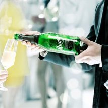 Eine elegante Hand reicht ein Glas Sekt, während eine andere Hand eine Flasche Champagner hält, um einen festlichen Moment zu feiern.