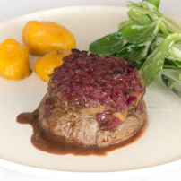 Ein saftiges Stück Rinderfilet, garniert mit einer roten Zwiebelmischung, serviert mit Kartoffeln und frischem Salat.