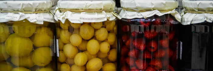 Vier Gläser mit eingelegtem Obst, darunter gelbe und rote Früchte, die mit weißen Deckeln abgedeckt sind.