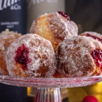 Eine verführerische Anordnung von Krapfen, die mit Puderzucker bestäubt und mit roter Marmelade gefüllt sind, auf einem Tisch präsentiert.