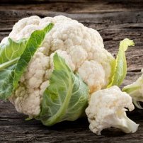 Ein frischer Blumenkohl liegt auf einer rustikalen Holzoberfläche, umgeben von grünen Blättern.