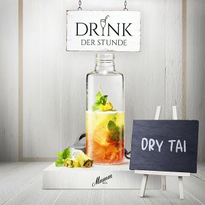 Ein eleganter Glasbehälter mit einem bunten Getränk, garniert mit frischer Minze und einer Ananasscheibe, steht auf einem weißen Tisch.