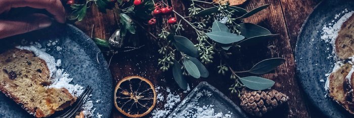 Ein rustikaler Tisch mit zwei Tellern, auf denen saftiger Kuchen und dekorative Pflanzen liegen, schafft eine gemütliche Atmosphäre.