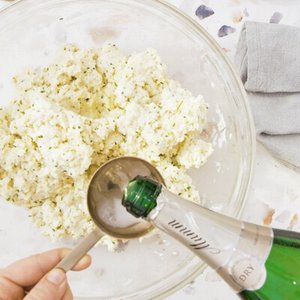 In einer transparenten Schüssel befindet sich eine fluffige Mischung, während ein Glas Sekt mit einem Löffel gefüllt wird.