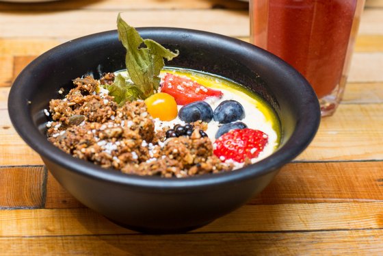 Eine schwarze Schüssel mit cremigem Joghurt, garniert mit frischen Beeren, Nüssen und einem Hauch von Minze.