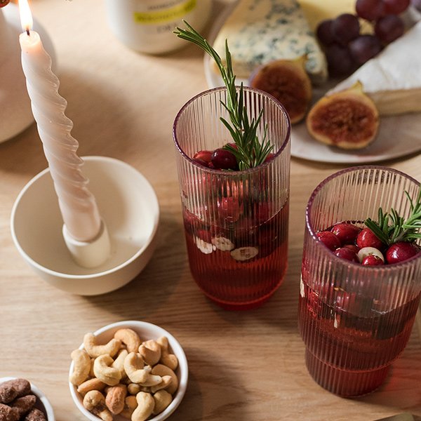 Ein rustikaler Tisch mit zwei dekorativen Gläsern, gefüllt mit Cranberries und frischen Kräutern, sowie einer brennenden Kerze.