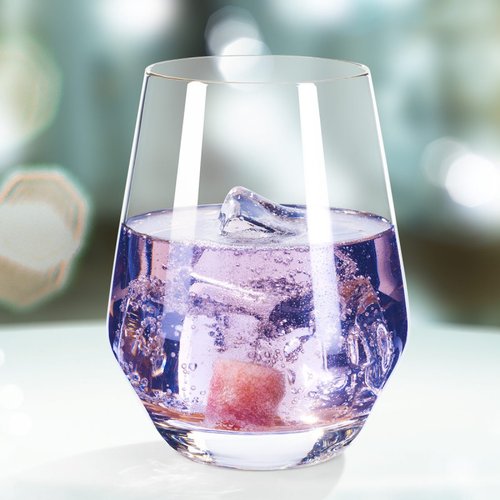 Ein elegantes Glas mit lila Getränk, gefüllt mit Eiswürfeln und einem Stück Frucht, vor einem verschwommenen Hintergrund.