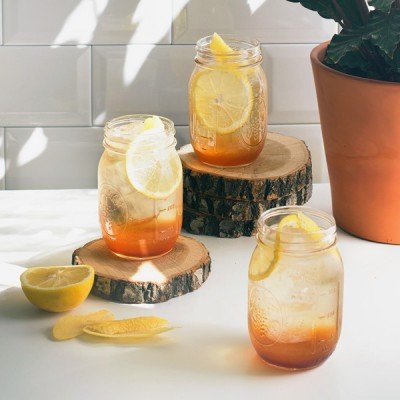 Drei Gläser mit Eistee stehen auf Holzscheiben, dekoriert mit Zitronenscheiben und umgeben von frischen Zitronen.