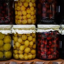 Ein Regal mit mehreren Gläsern, gefüllt mit bunten eingelegten Früchten, darunter gelbe und rote Sorten, die appetitlich aussehen.