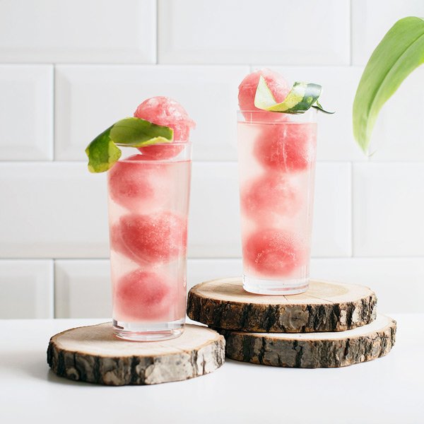 Zwei hohe Gläser mit Wassermelonen-Sorbet, dekoriert mit Limettenblättern, stehen auf Holzscheiben.