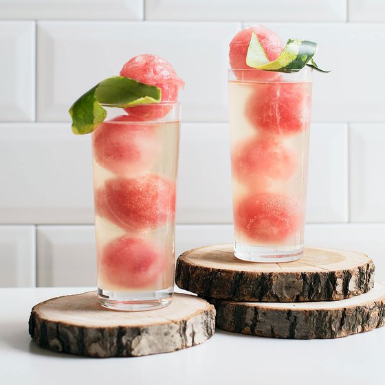 Zwei hohe Gläser mit sprudelndem Getränk, gefüllt mit Wassermelonenbällchen und garniert mit Limettenblättern.