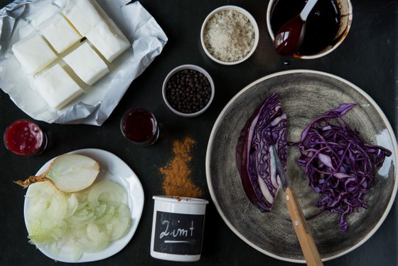 Auf einem Tisch liegen frische Zutaten, darunter violetter Kohl, Zwiebeln und Gewürze, bereit zum Kochen.
