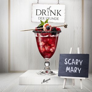 Ein elegantes Glas mit einem roten Getränk, garniert mit Beeren und Minze, steht vor einem Schild mit der Aufschrift 'Scary Mary'.
