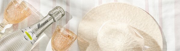 Eine Flasche alkoholfreier Sekt steht neben zwei eleganten Gläsern auf einem gestreiften Tischläufer.